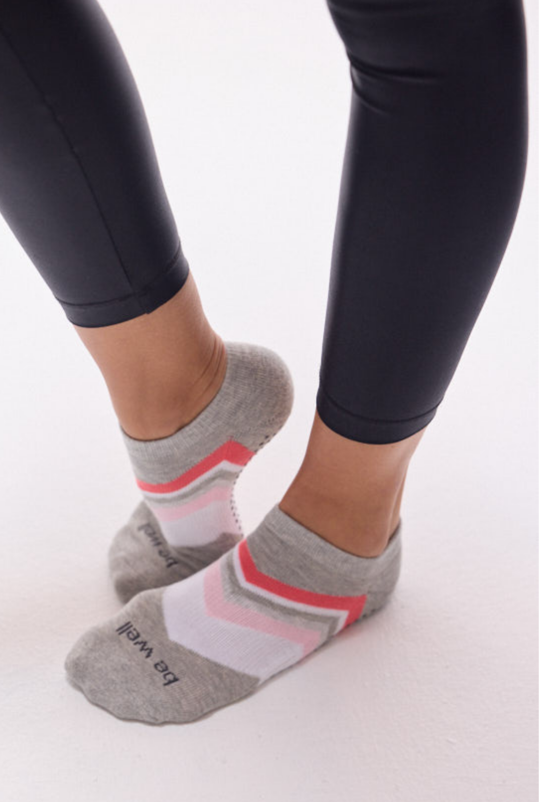 Gray ankle socks with pink and white stripes worn with black leggings on a white background